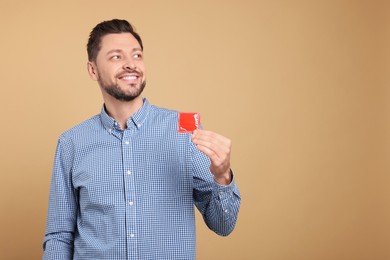 Happy man holding condom on beige background. Space for text