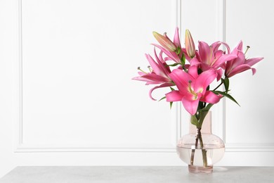 Photo of Beautiful pink lily flowers in vase on light grey table against white wall, space for text