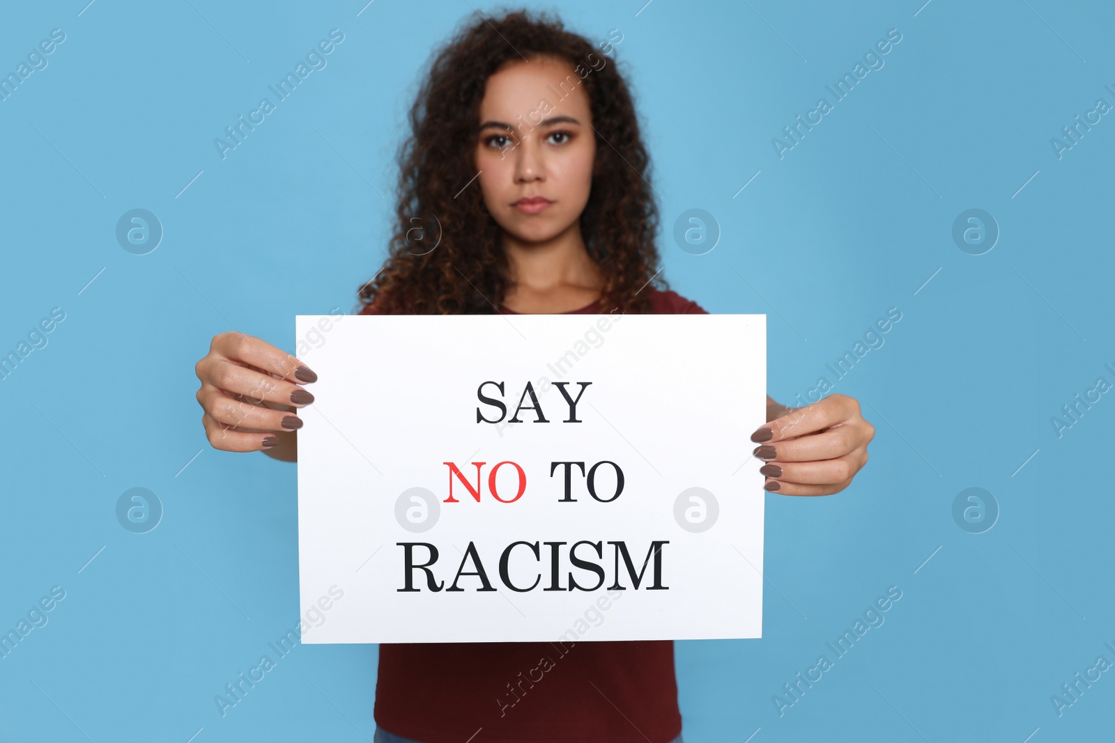 Photo of African American woman holding sign with phrase Say No To Racism against light blue background, focus on hands