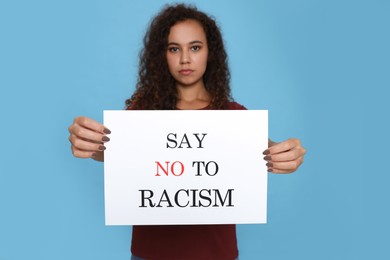 Photo of African American woman holding sign with phrase Say No To Racism against light blue background, focus on hands