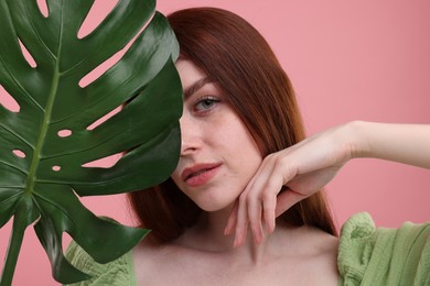 Portrait of beautiful woman with freckles and monstera leaf on pink background