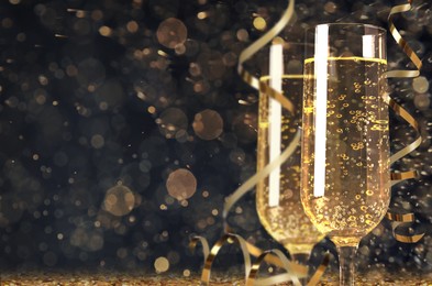 Image of Glasses with sparkling wine and shiny serpentine streamers against blurred festive lights, space for text