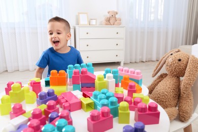 Photo of Cute little boy playing with colorful building blocks at table in room