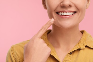Woman pointing at her clean teeth and smiling on pink background, closeup