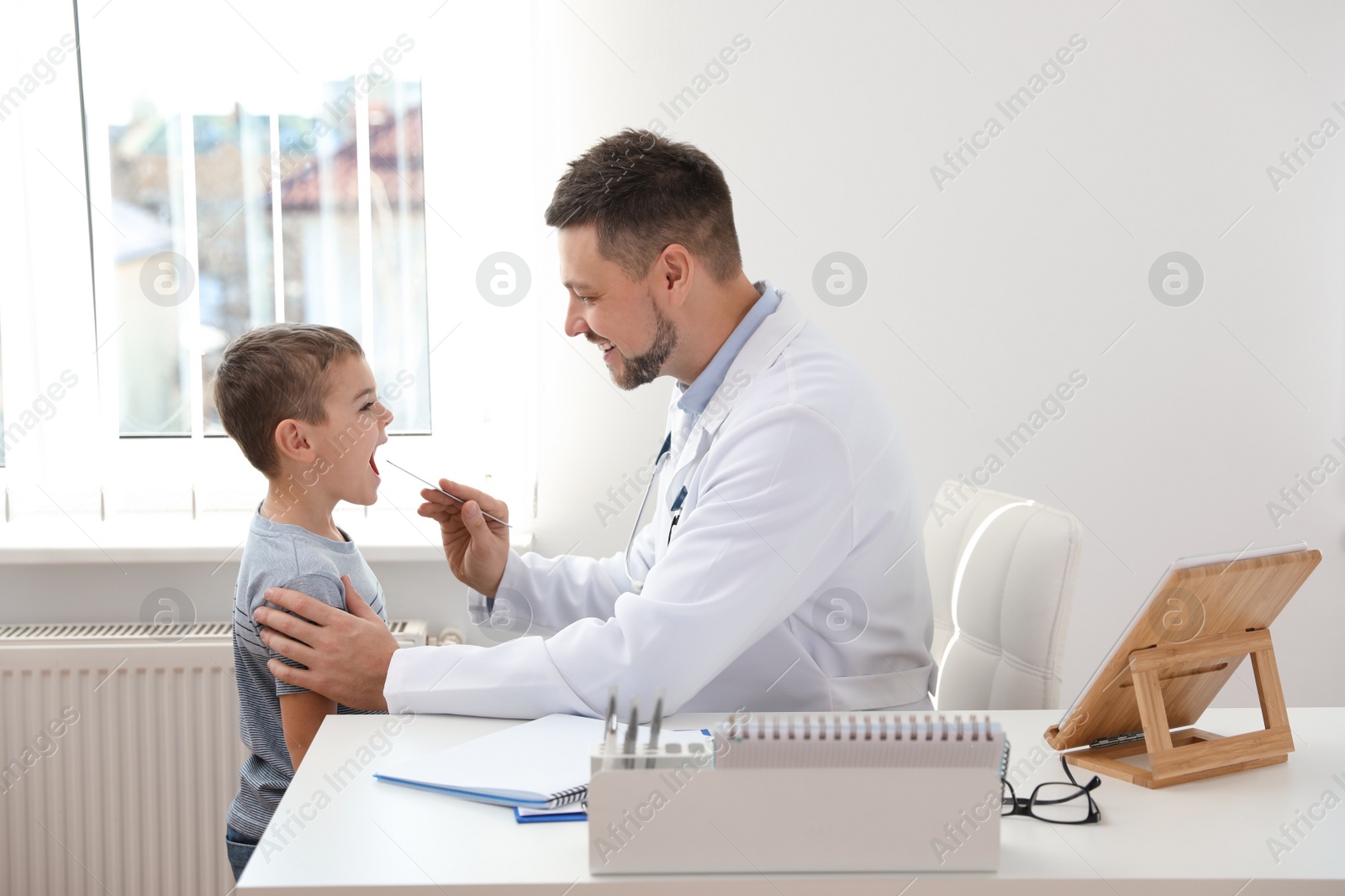 Photo of Children's doctor examining little patient's throat in clinic