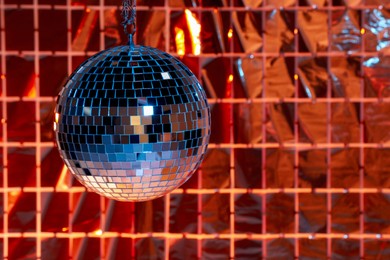 Photo of Shiny disco ball against foil party curtain under color lights, space for text