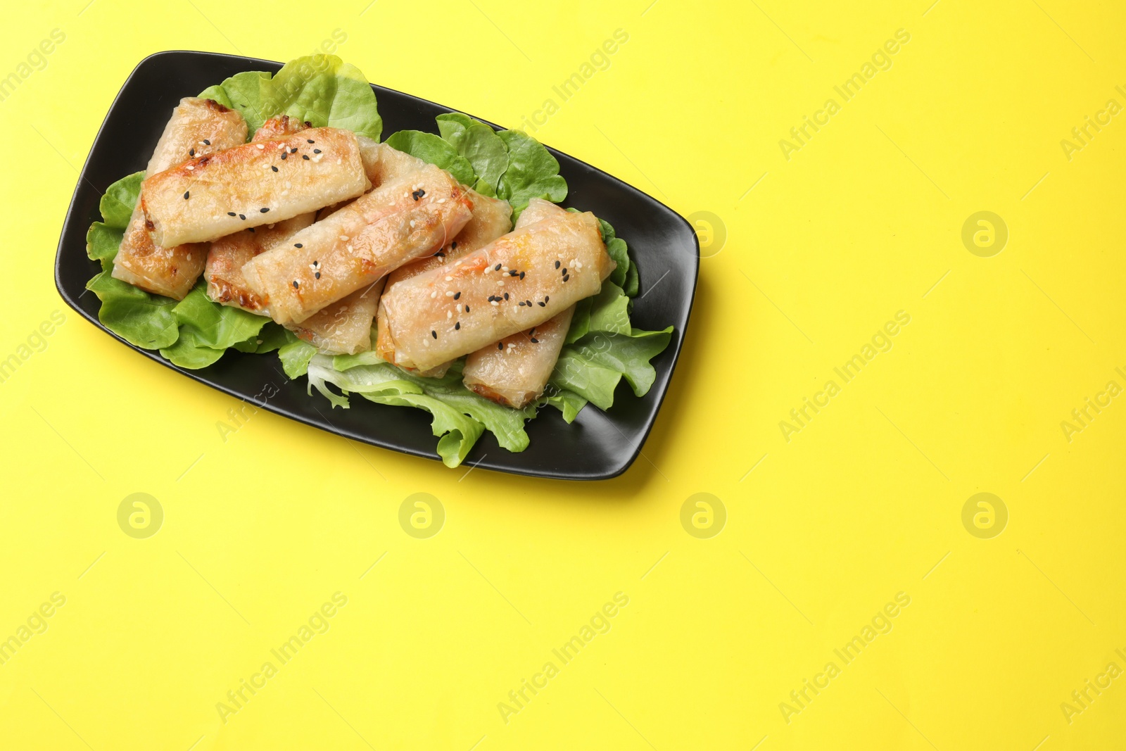 Photo of Tasty fried spring rolls and lettuce on yellow table, top view. Space for text