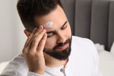 Man with dry skin applying cream onto his forehead indoors