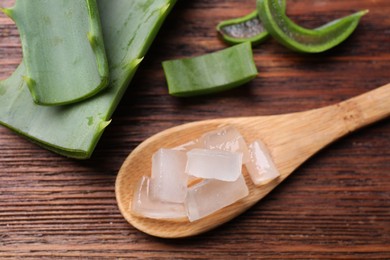 Aloe vera gel and slices of plant on wooden table, flat lay