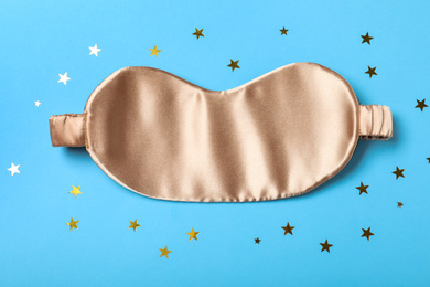 Photo of Beige sleeping mask and glitter on light blue background, flat lay. Bedtime accessory
