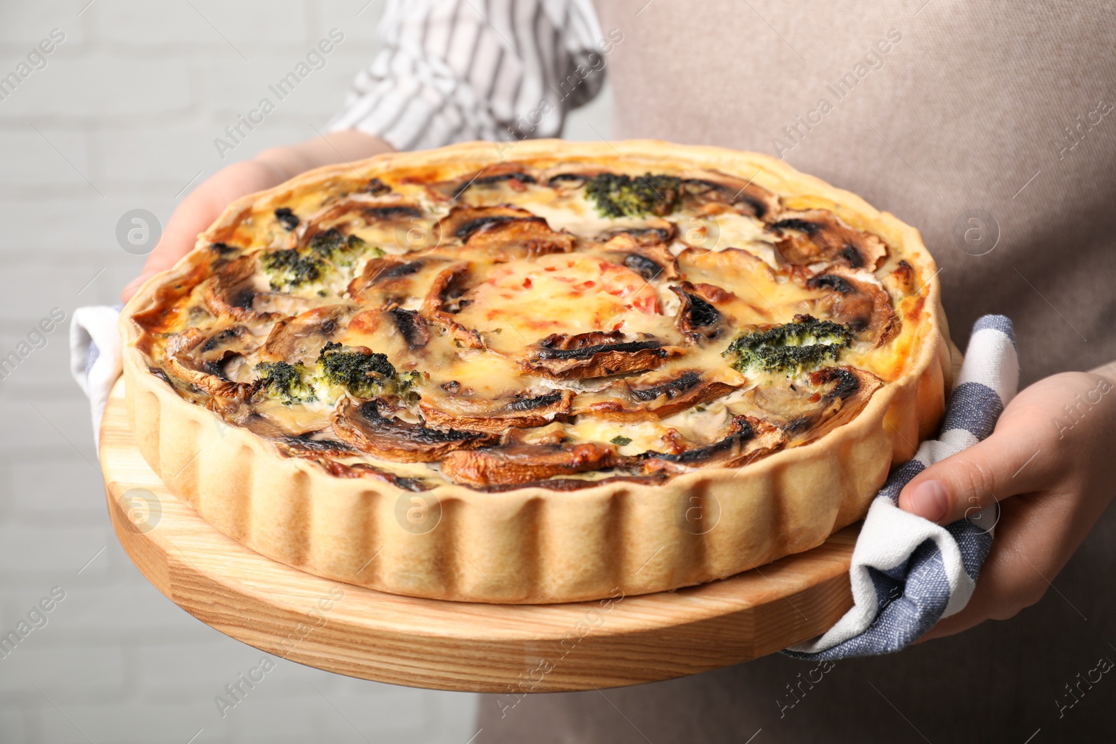 Photo of Woman holding delicious homemade quiche with mushrooms near white brick wall, closeup