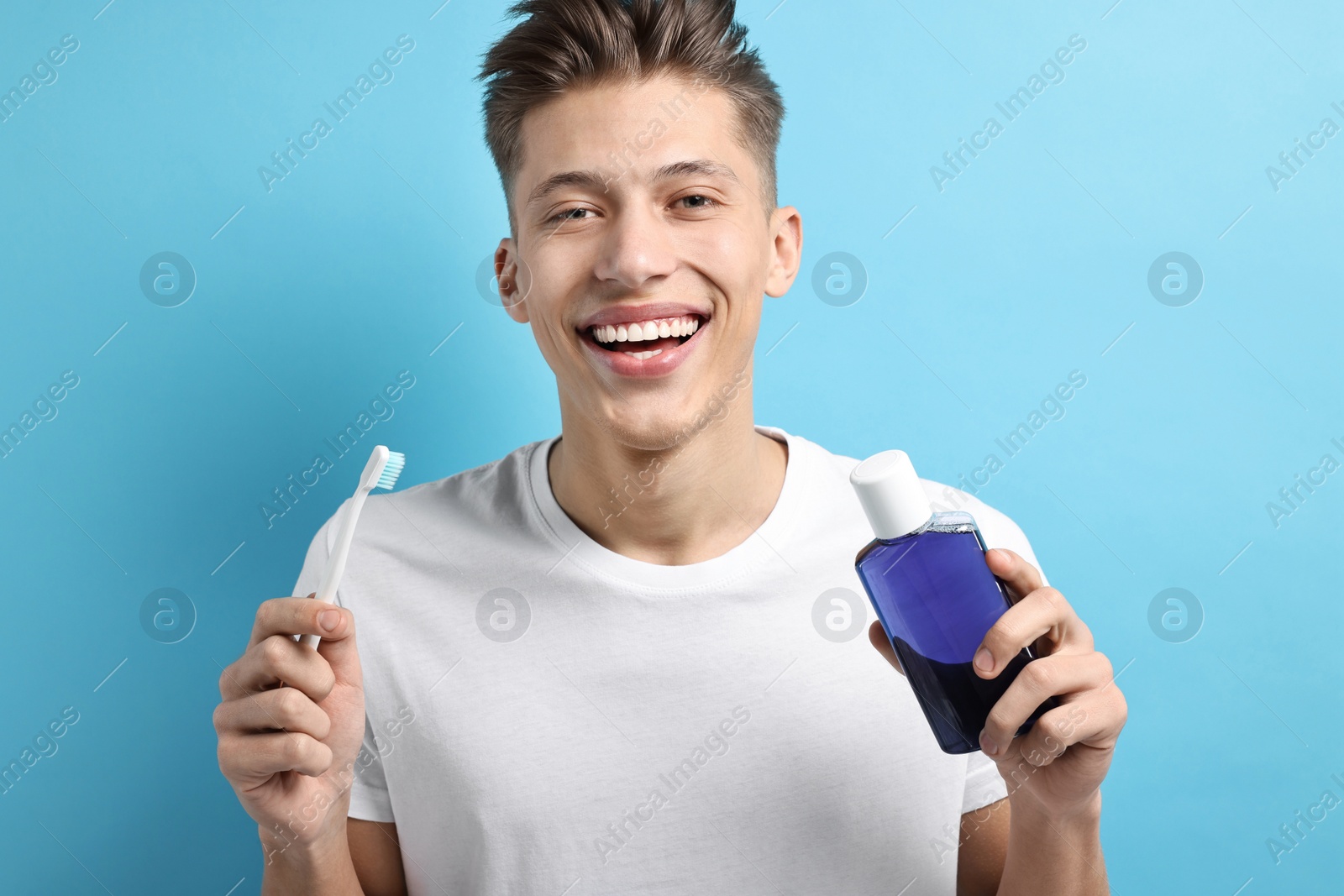 Photo of Young man with mouthwash and toothbrush on light blue background