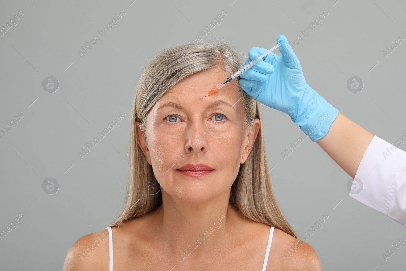 Photo of Doctor giving facial injection to senior woman on light grey background, closeup. Cosmetic surgery