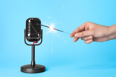 Photo of Woman making ASMR sounds with microphone and burning sparkler on light blue background, closeup