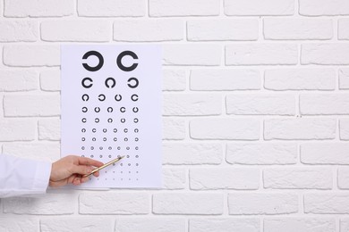 Ophthalmologist pointing at vision test chart on white brick wall, closeup. Space for text