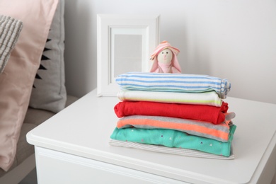 Photo of Toy bunny and stack of stylish child clothes on table indoors