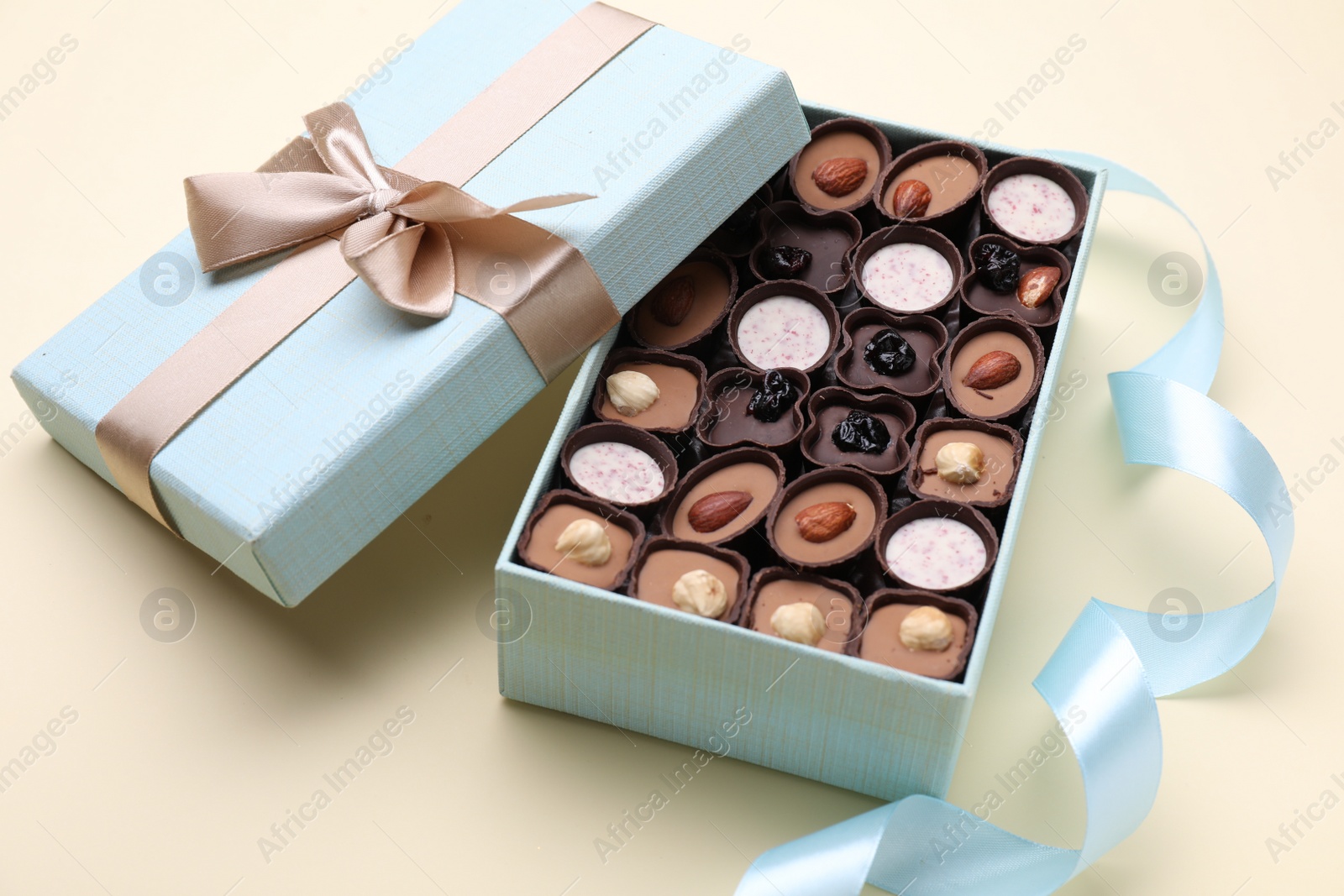 Photo of Open box of delicious chocolate candies and light blue ribbon on beige background