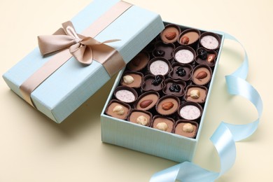 Open box of delicious chocolate candies and light blue ribbon on beige background