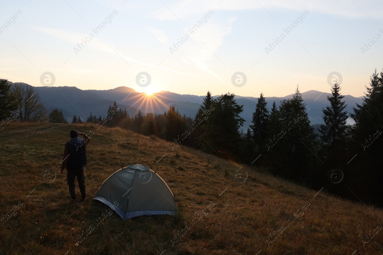 Photo of Tourist enjoying sunrise near camping tent in mountains, back view