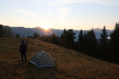Photo of Tourist enjoying sunrise near camping tent in mountains, back view