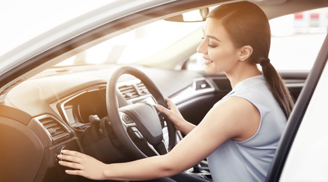 Image of Happy young woman driving modern car on sunny day