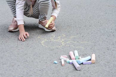 Photo of Little child drawing sun with chalk on asphalt, closeup
