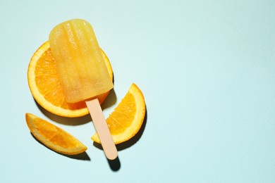 Photo of Tasty orange ice pop and space for text on pale light blue background, top view. Fruit popsicle