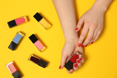 Woman with red manicure and nail polish bottles on color background, top view