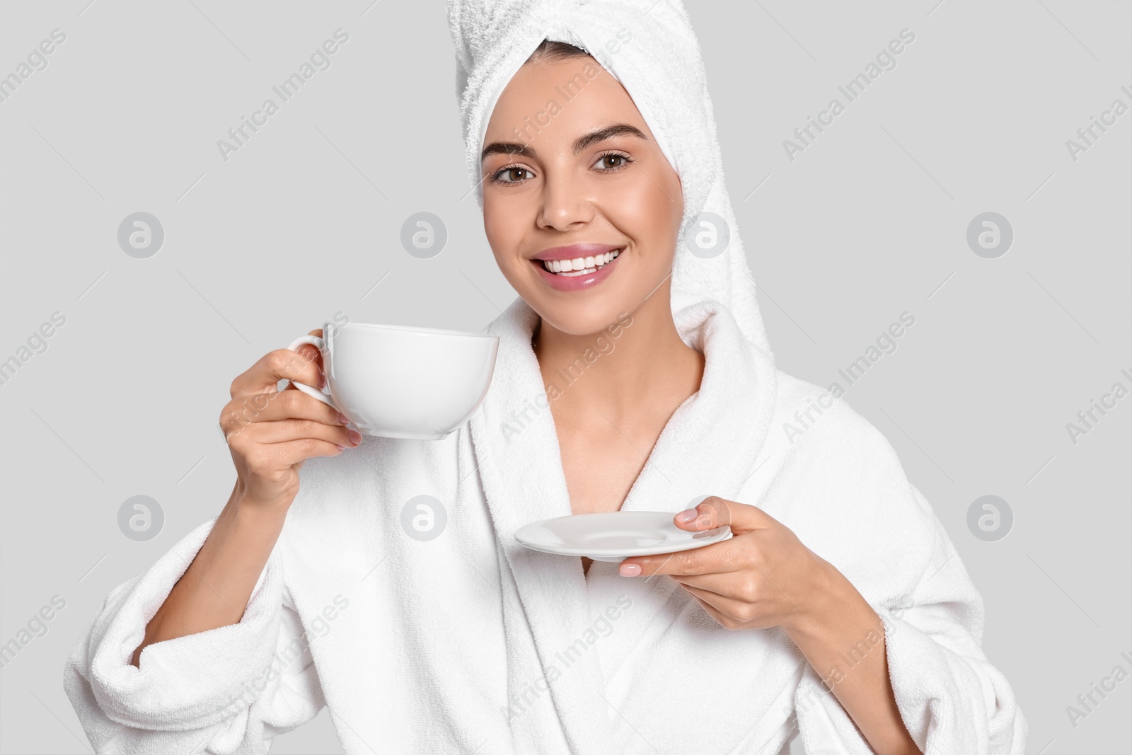 Photo of Young woman in bathrobe with towel and cup of drink on light grey background. Spa treatment