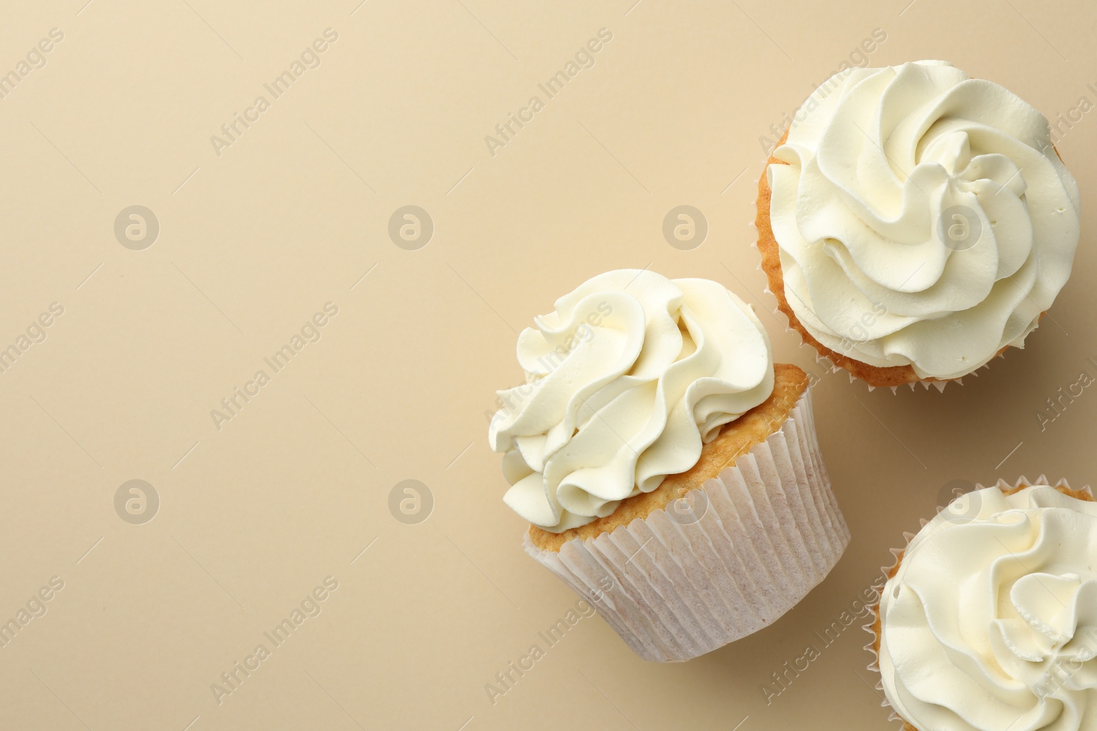 Photo of Tasty vanilla cupcakes with cream on beige background, top view. Space for text