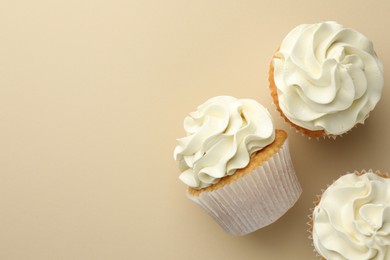 Tasty vanilla cupcakes with cream on beige background, top view. Space for text