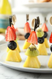 Photo of Tasty canapes with pineapple, kiwi and berries on white marble table, closeup
