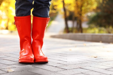 Photo of Woman wearing red rubber boots on paved street in park, closeup. Autumn walk