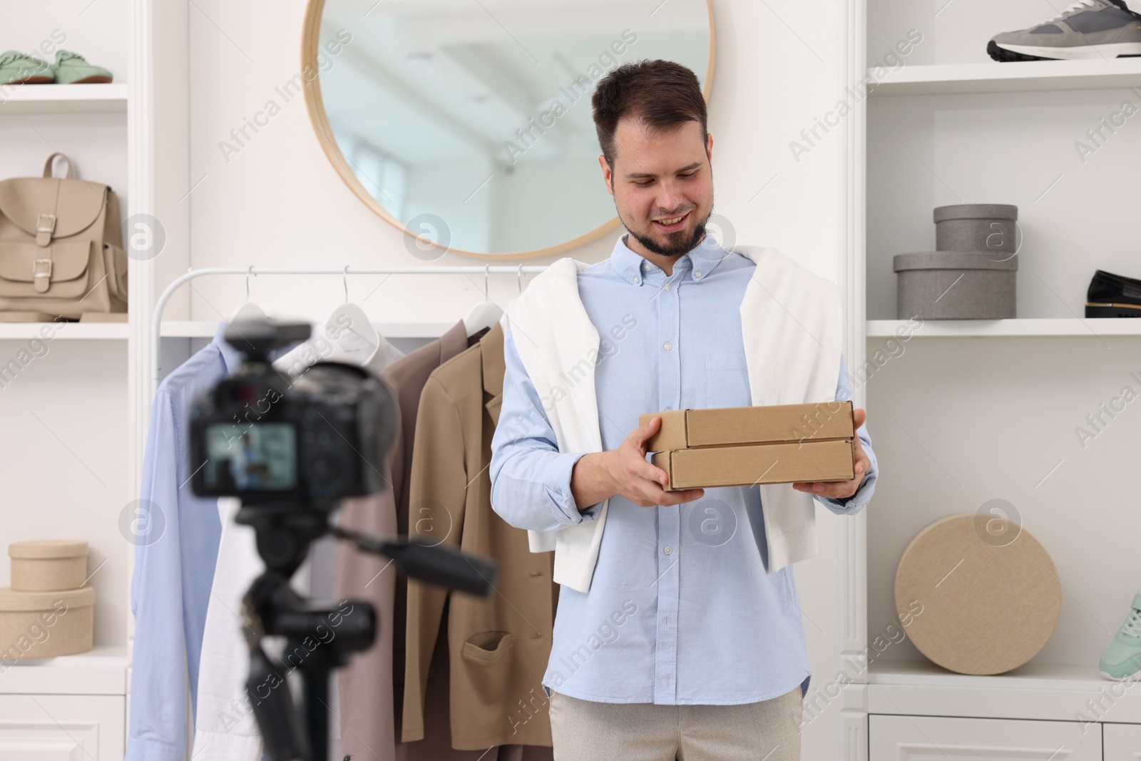 Photo of Smiling fashion blogger with cardboard boxes recording video at home