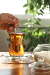 Woman stirring sugar in tea at wooden table indoors, closeup