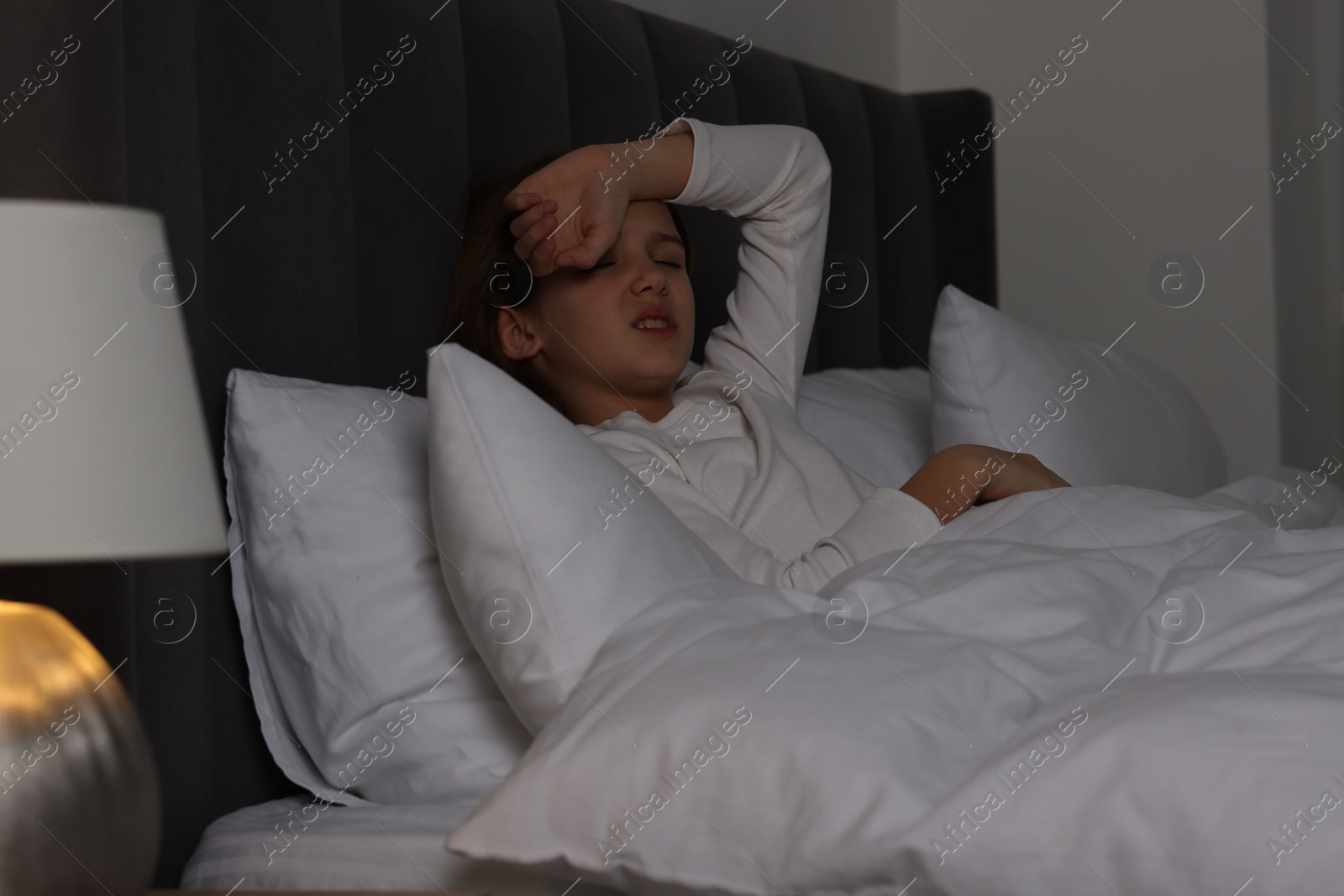 Photo of Little girl suffering from headache in bed at night