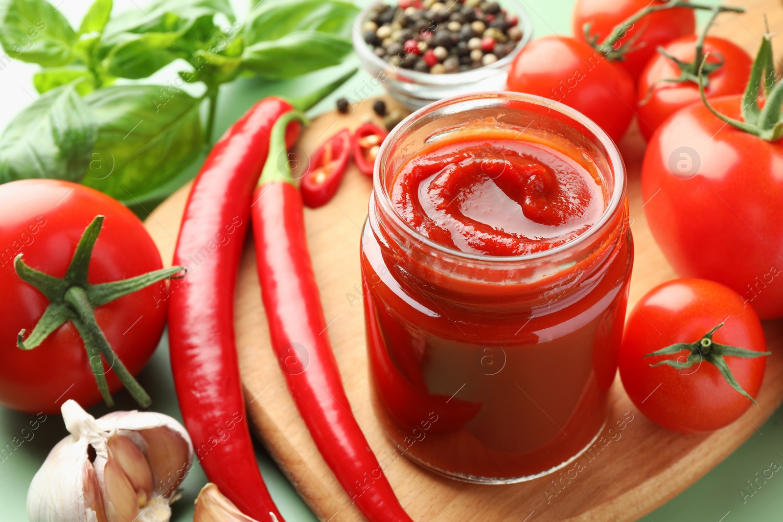 Photo of Jar of tasty ketchup and ingredients on green table, closeup