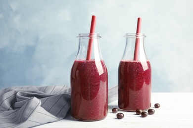 Bottles with delicious acai smoothie on table against color background