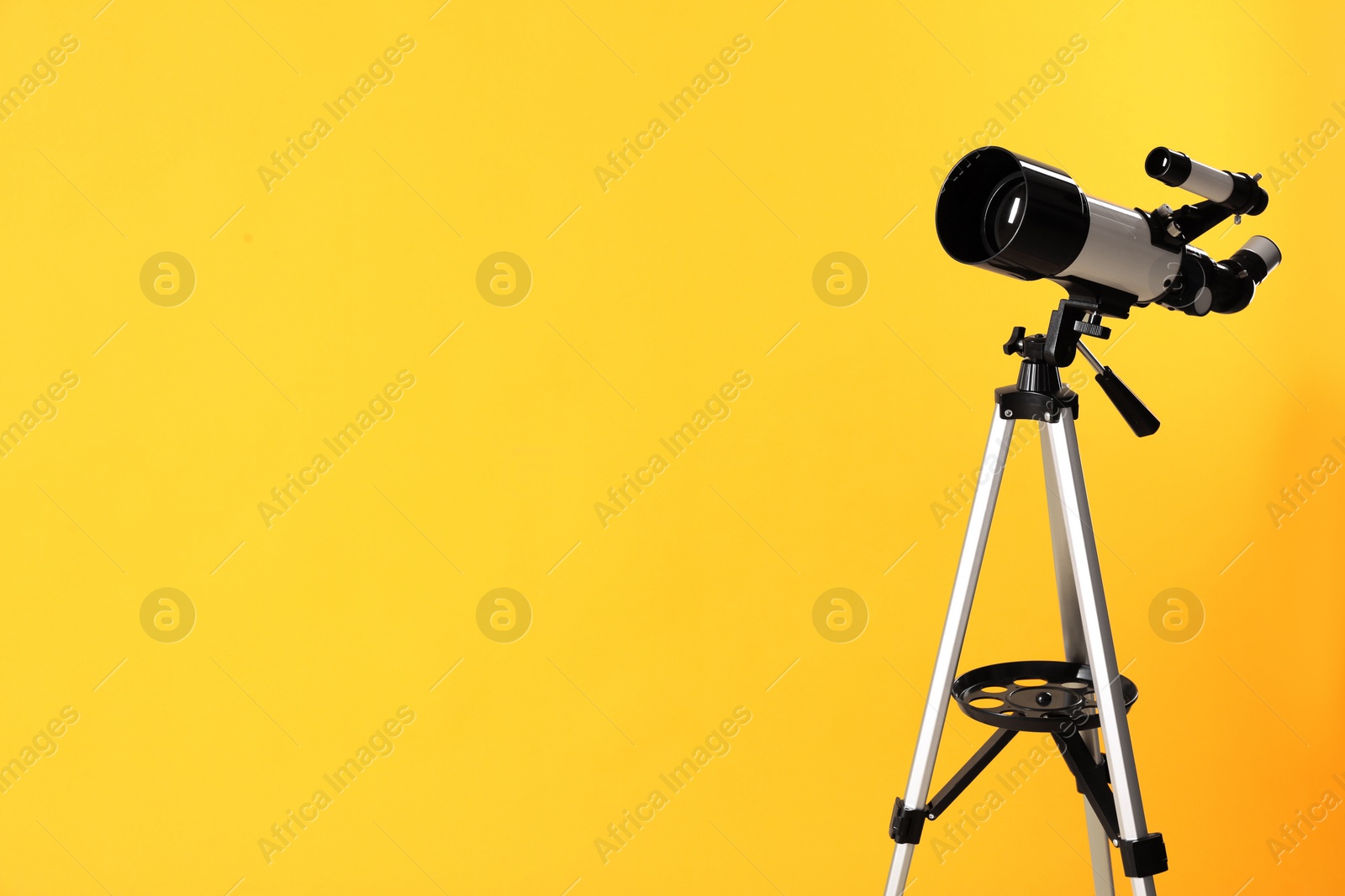 Photo of Tripod with modern telescope on yellow background. Space for text