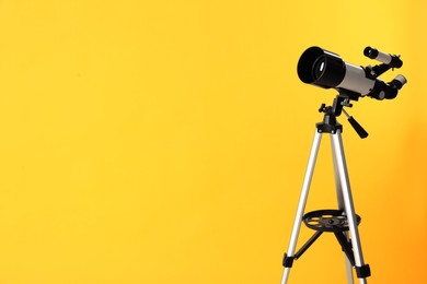 Photo of Tripod with modern telescope on yellow background. Space for text