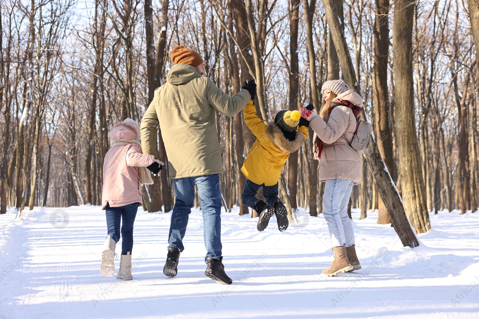 Photo of Family walking in sunny snowy forest, back view