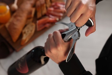 Photo of Romantic dinner. Man opening wine bottle with corkscrew at table indoors, above view
