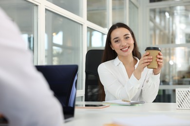 Photo of Happy woman with paper cup of coffee at desk in open plan office