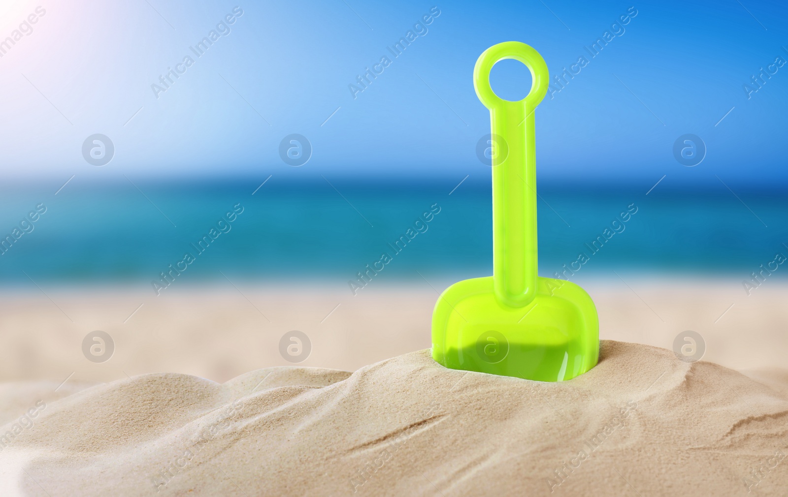 Image of Green plastic toy shovel sandy beach near sea, space for text 