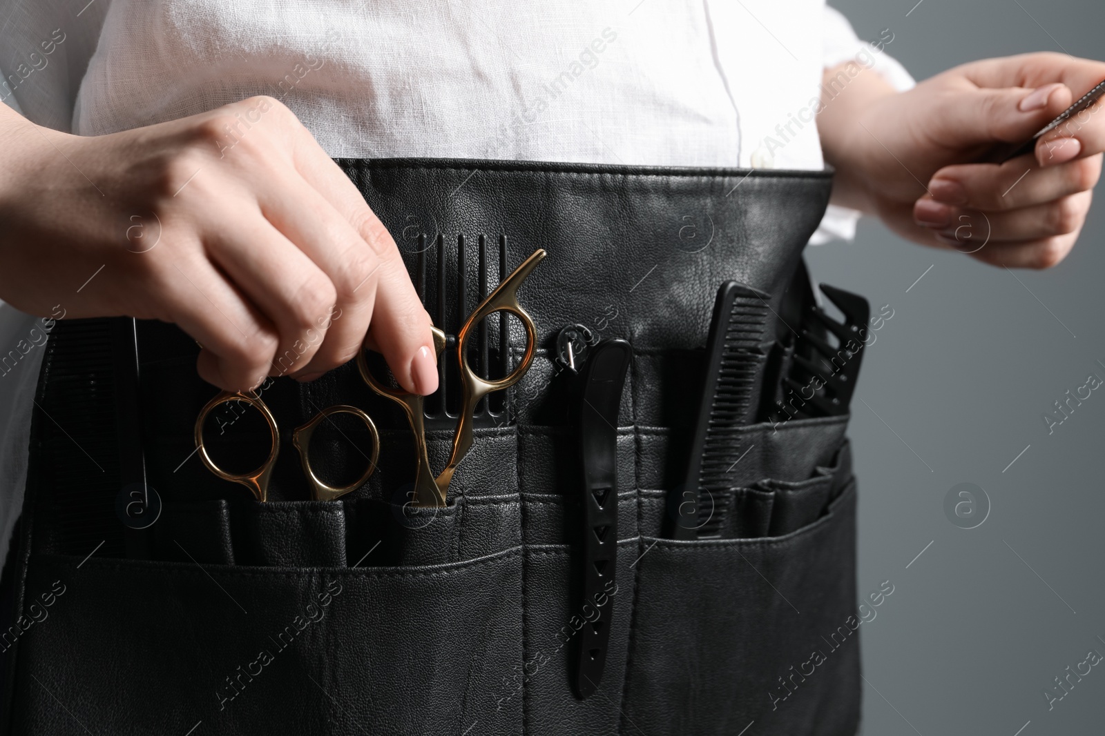 Photo of Hairstylist with professional tools in waist pouch on grey background, closeup