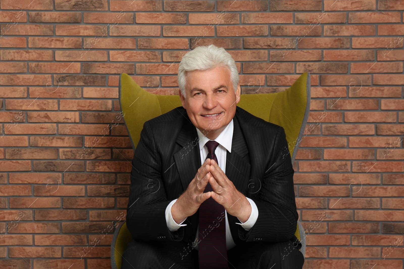 Photo of Happy mature businessman sitting in armchair near brick wall