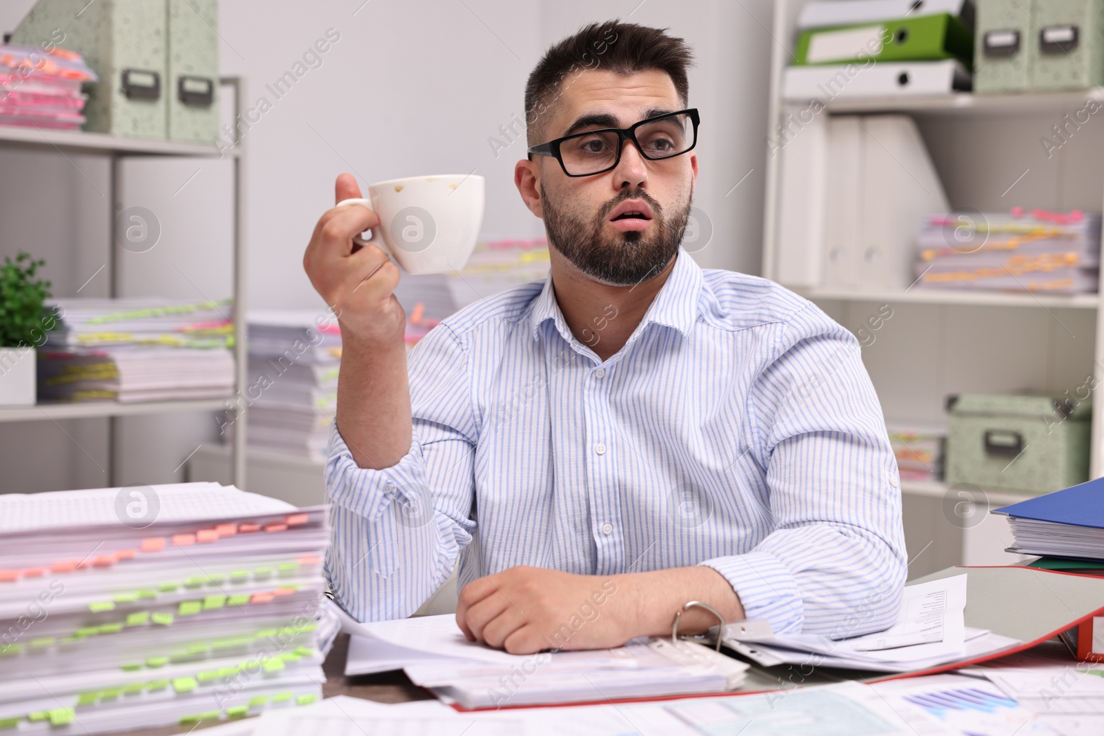 Photo of Overwhelmed man with cup of drink at table in office