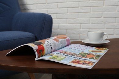 Photo of Open magazine and cup of coffee on wooden table in room
