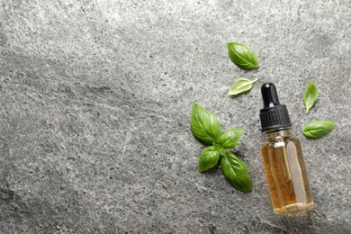 Photo of Glass bottle of basil essential oil and leaves on grey stone table, flat lay. Space for text