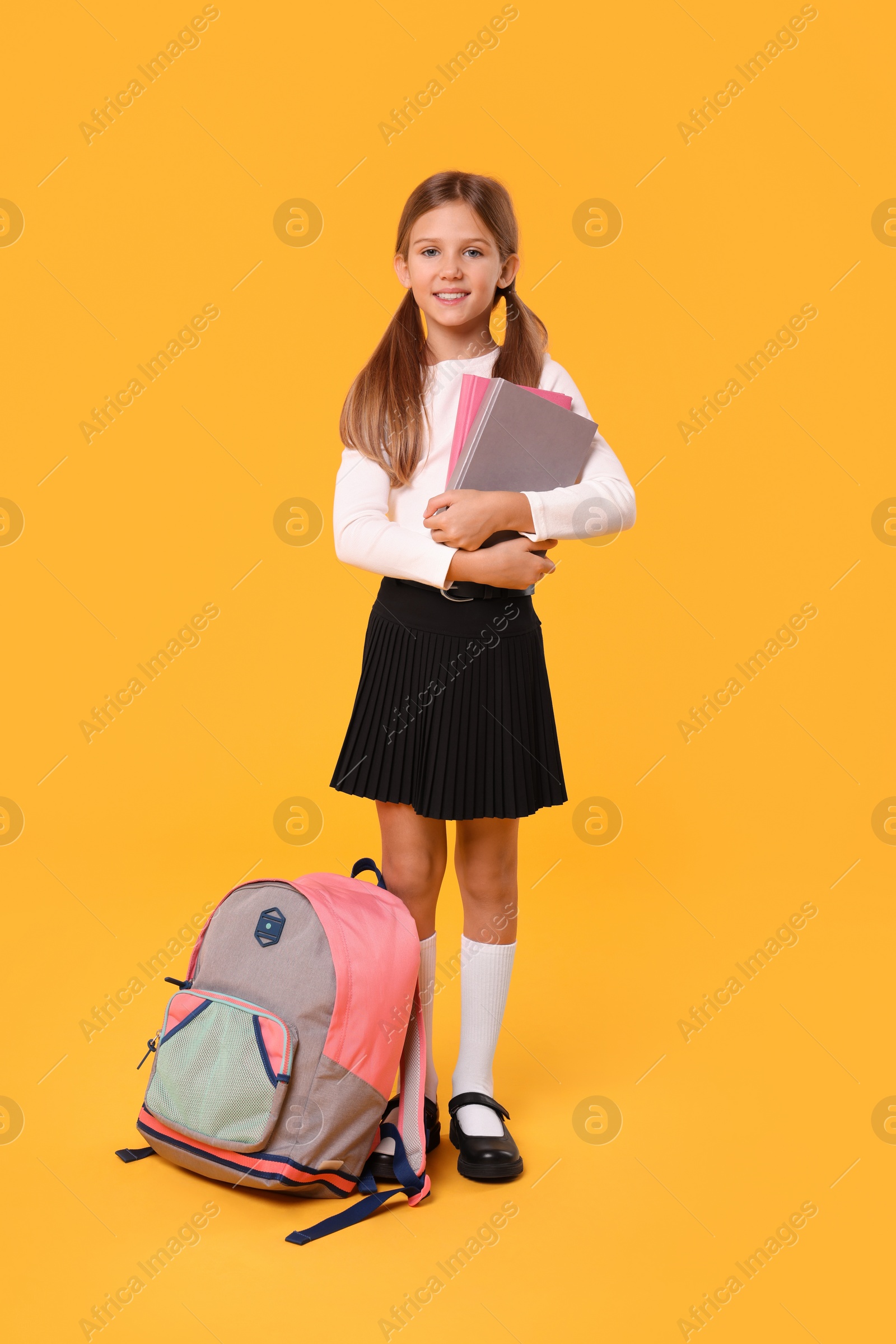 Photo of Happy schoolgirl with backpack and books on orange background